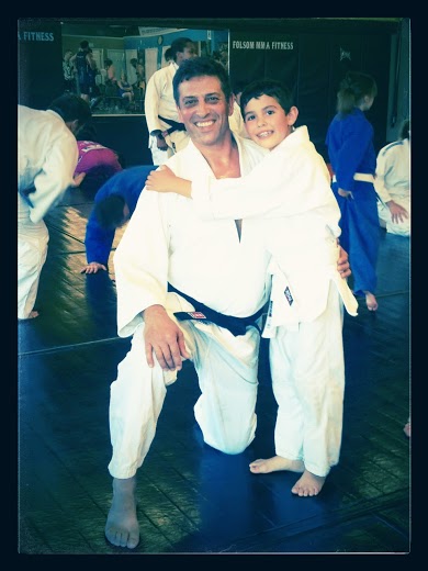 Coach Pedro Teixera kneeling on the mat with his arm around a young student